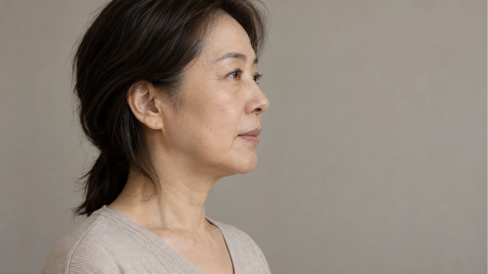 턱선과 목이 함께 보이는 옅은 회색 상의 성인의 반측면 얼굴