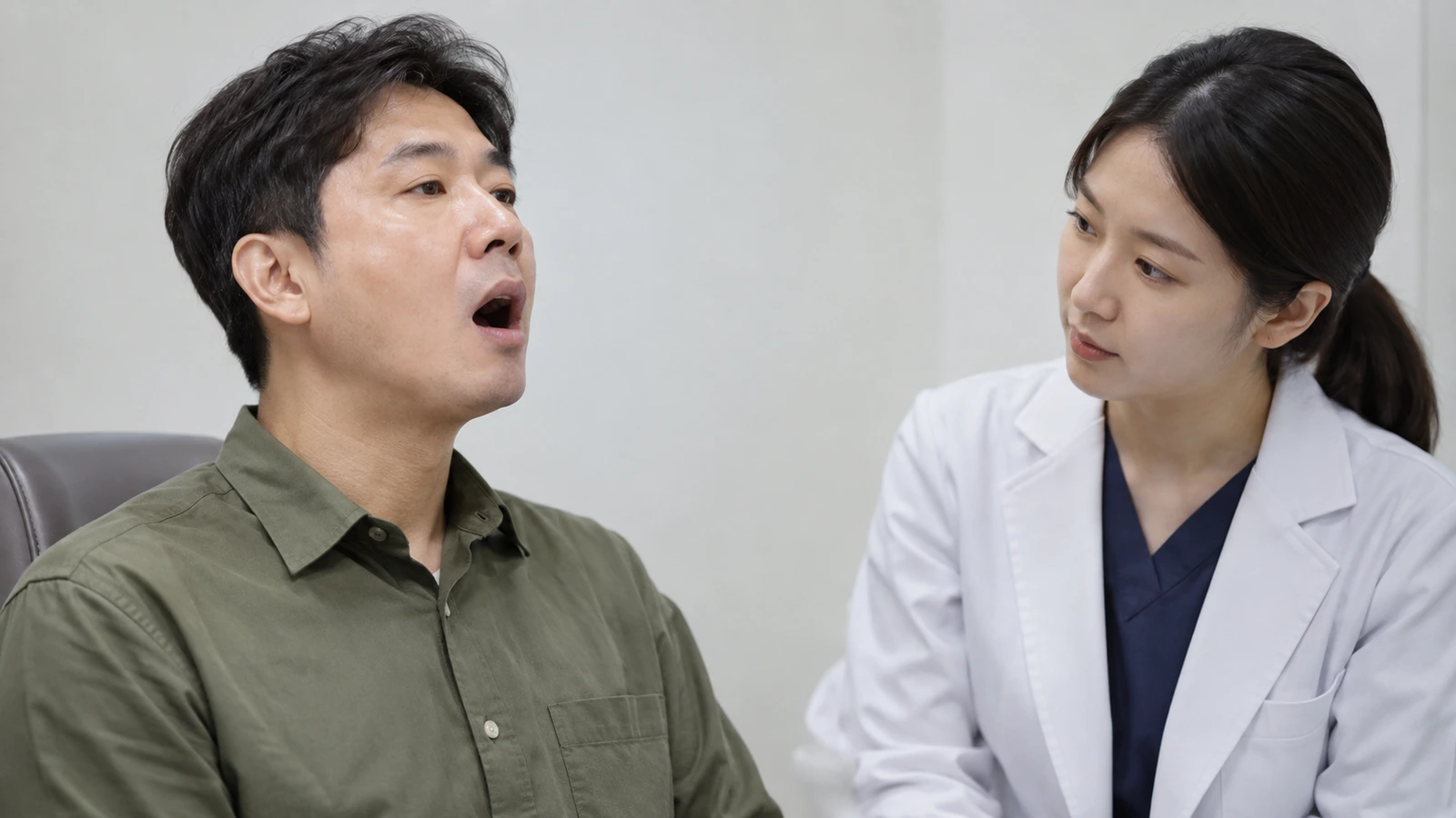 입을 벌린 성인 남성의 얼굴을 흰 가운을 입은 의료진이 바라보는 모습